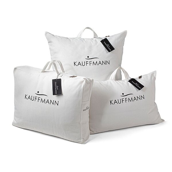 Drei Tragetaschen in weiß mit dem KAUFFMANN Logo in schwarz und schwarzen Produktetiketten.