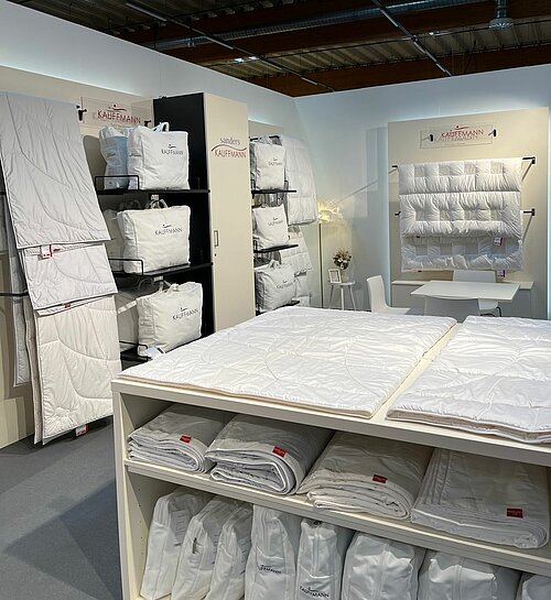 Messestand auf der Hometex 2025 mit beigen Standelementen und präsentierten Bettdecken.