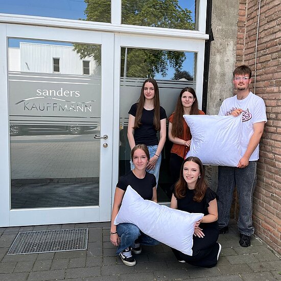 Cinq apprentis posent pour une photo de groupe ; trois sont debout, deux sont accroupis devant eux, tous regardent l'appareil photo.