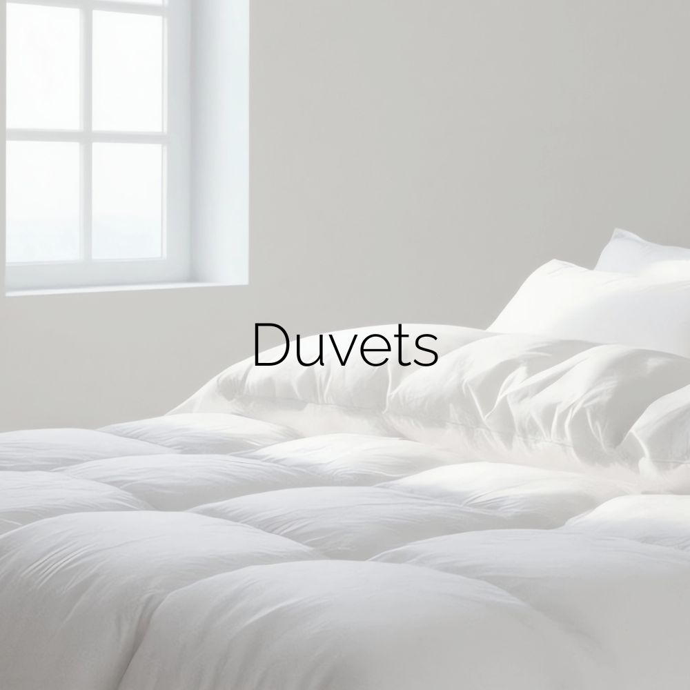 Bed with white duvet and white pillows without covers. Image caption: “Duvets.”